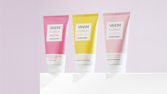 drei Handcremetuben in pink, gelb und rosa stehen nebeneinander auf einem weißen Podest